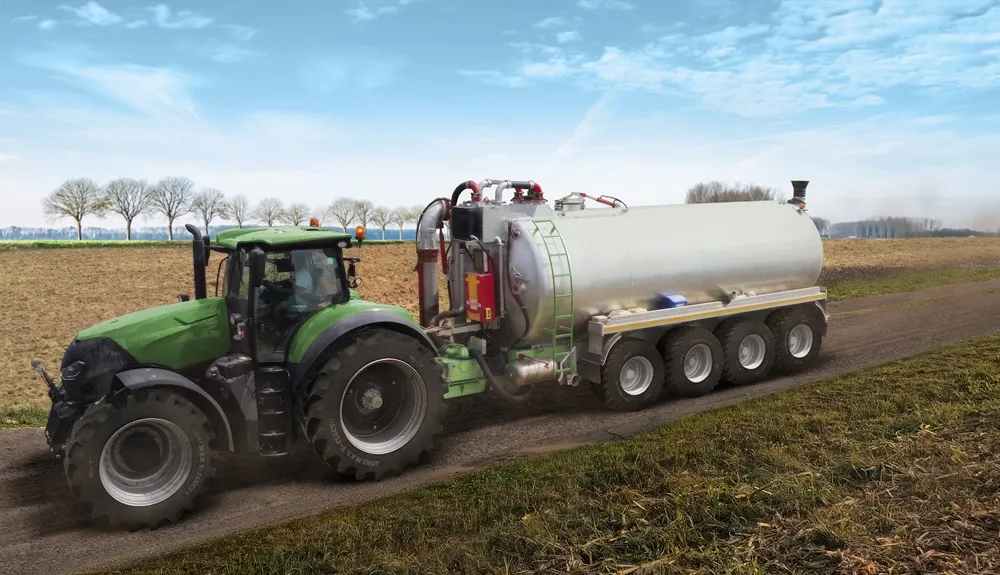 Green tractor in a field pulling a tanker-style trailer