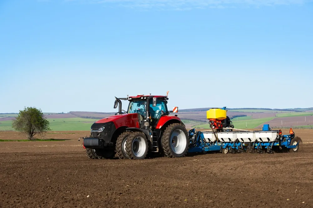 Image of a red tractor ploughing a field with a blue sky background