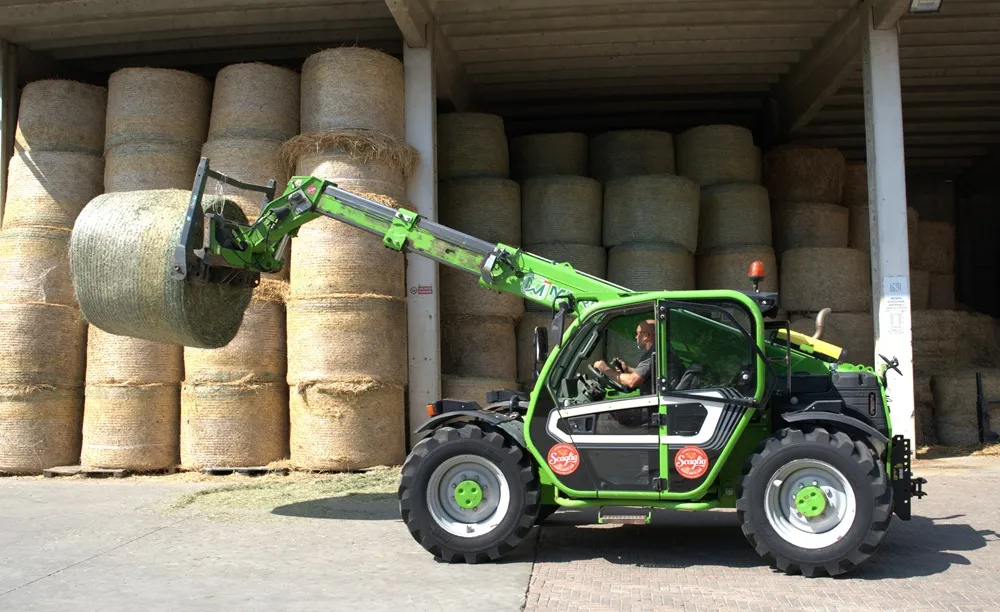 Farming machinary lifting a bail in fron t over other bails