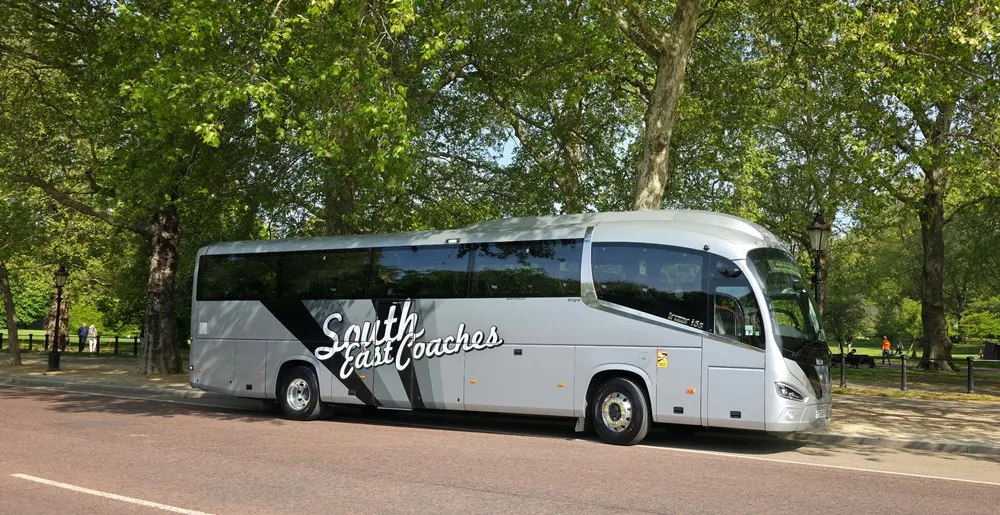 Image of a South East Coach in silver, parked in front of some trees with green leaves.